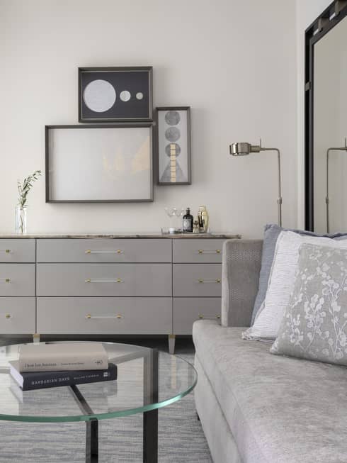 Guest room with silver couch, glass coffee table, grey chest of drawers, and art decor