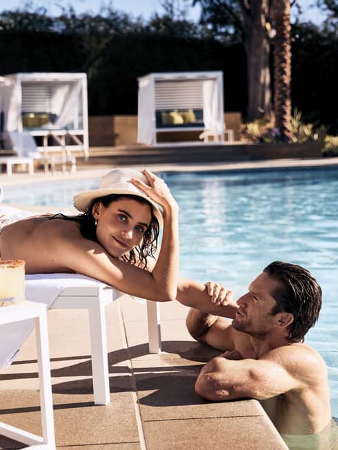 Guest laying in a lounge chair by the pool while the other guest stands in the pool.