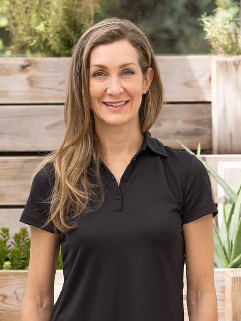 A woman in a black shirt standing in front of a wooden fence.
