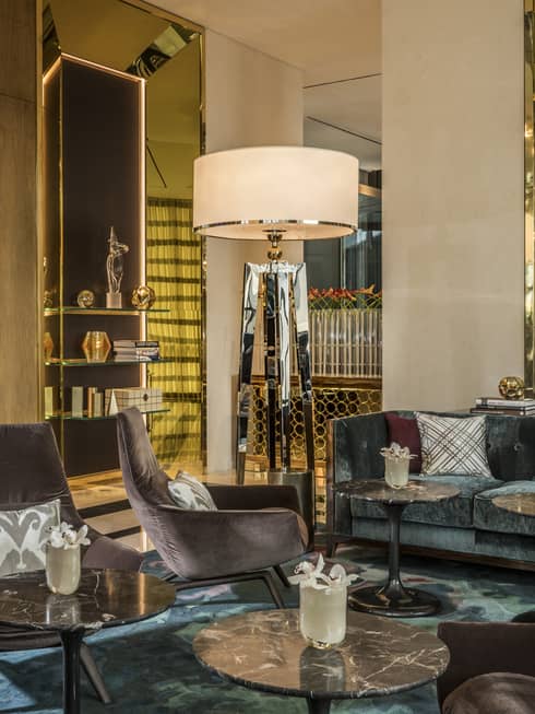 Penrose Lounge seating area with mid-century style velvet armchairs, accent pillows, tall lamps
