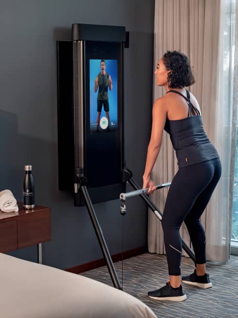 Woman exercises in front of an instructor on a screen in a Tonal technology-equipped guest room