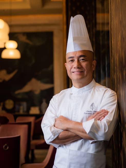 Chef Cheung stands with his arms crossed in front of several set tables.