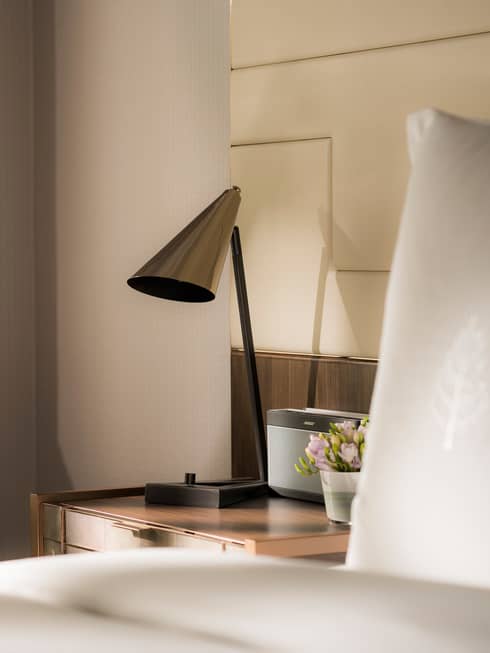 Modern silver lamp on nightstand beside alarm clock, bed