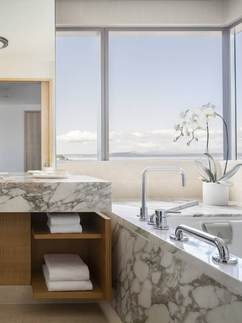 A marble tub and countertops are accented by flowers and multiple windows