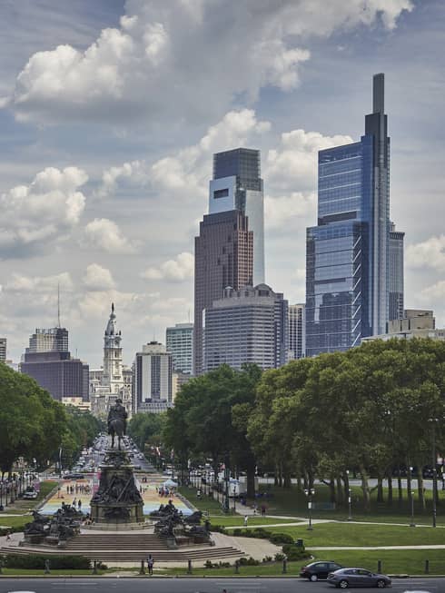 Skyscrapers over city park, statues and road