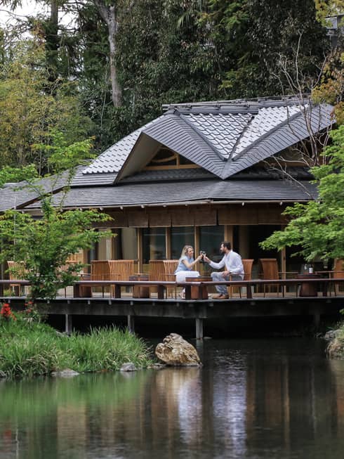 View across pond to restaurant patio where couple toasts with wine glasses