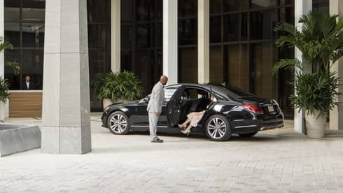 Entrance of Four Seasons Hotel New Orleans featuring a modern glass canopy, sleek architecture, and a welcoming fountain, with a luxury car and valet service in front.