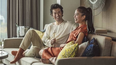 Two people sitting on a sofa, smiling and enjoying a drink together