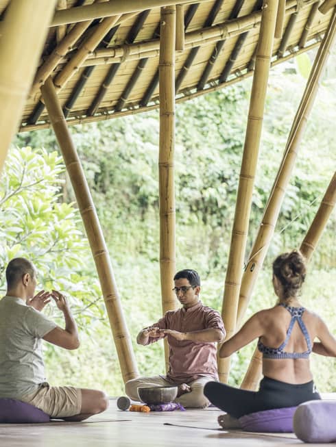 Group meditates on outdoor pavilion platform with bamboo poles