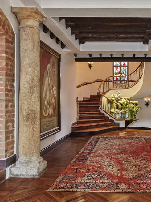 Rustic pillars, oriental carpet leading to winding staircase, table with vases with fresh white flowers