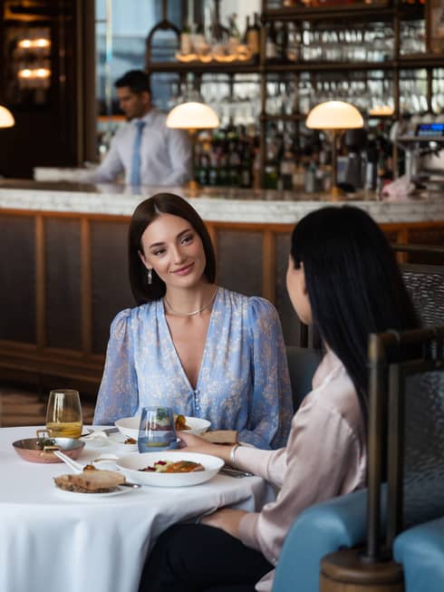 Two women sitting at a round dining table in the center of a restaurant