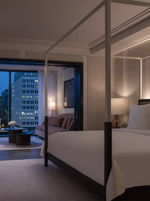 Presidential Suite dimly lit and with all-white modern four-poster bed and evening balcony view