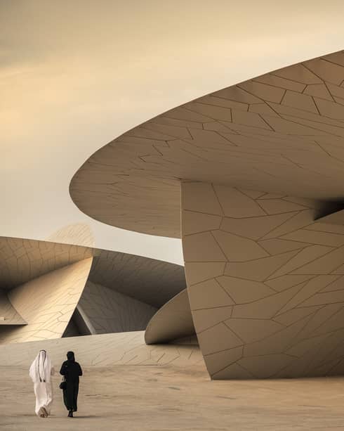 Two people walk beside a giant modern structure featuring large, overlapping, disc-shaped forms with geometric patterns. 
