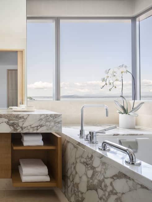 A marble tub and countertops are accented by flowers and multiple windows