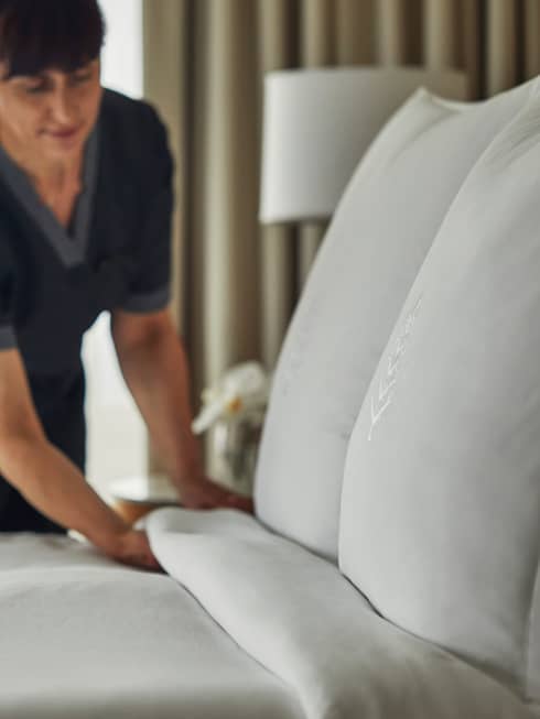 Hotel housekeeping staff makes bed, white linens and pillows