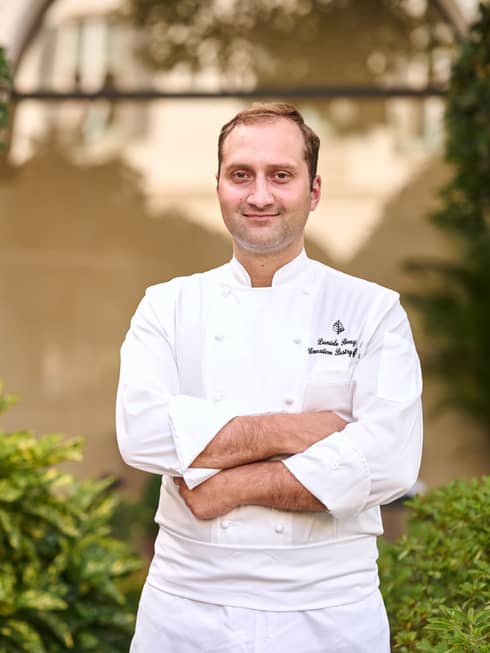 A chef outside nears bushes and trees in white chef's clothes.