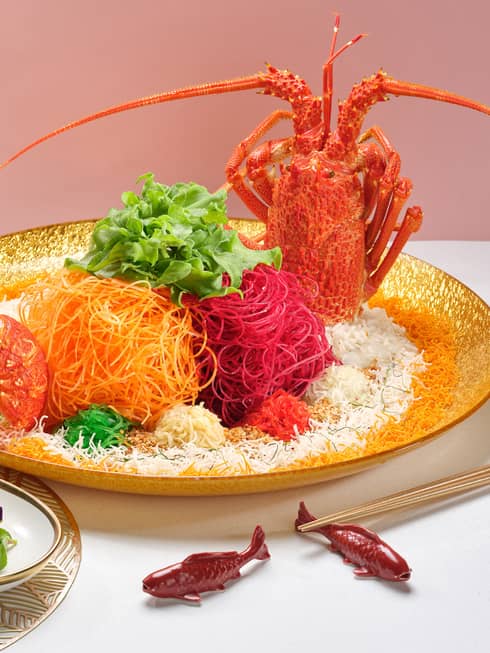 Colourful traditional Lunar New Year dish with whole lobster, shredded carrots and beets, dipping sauces and edible flowers