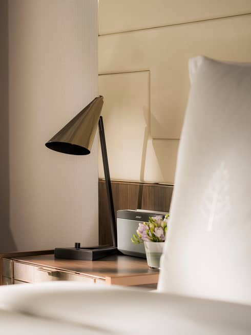 Modern silver lamp on nightstand beside alarm clock, bed