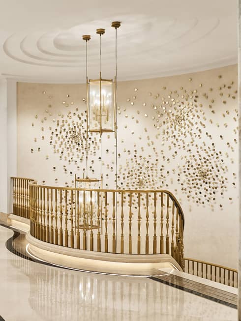 Top of a gold-railing staircase, with many small brass dots on the wall as art