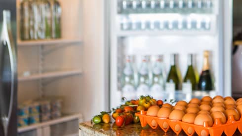 Smiling man holds green bottle in front of open fridge, fresh eggs on counter