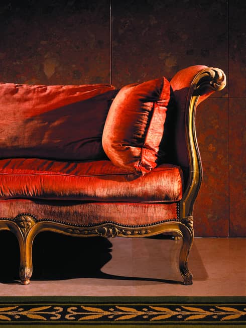 Close up of one end of antique style red velvet sofa in dark room