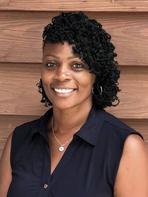 A woman in a black blouse standing in front of a wood wall.