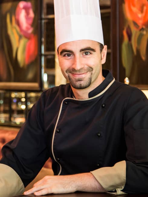 Portrait photo of Chef Valerio Andrisani wearing black uniform, tall white hat