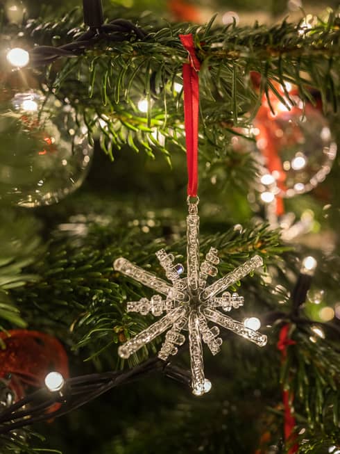 Close-up of a crystal snowflake ornament hanging on a Christmas tree with festive lights in the background