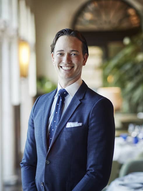 Portrait photo of smiling man in tailored suit and tie, formal dining room in background