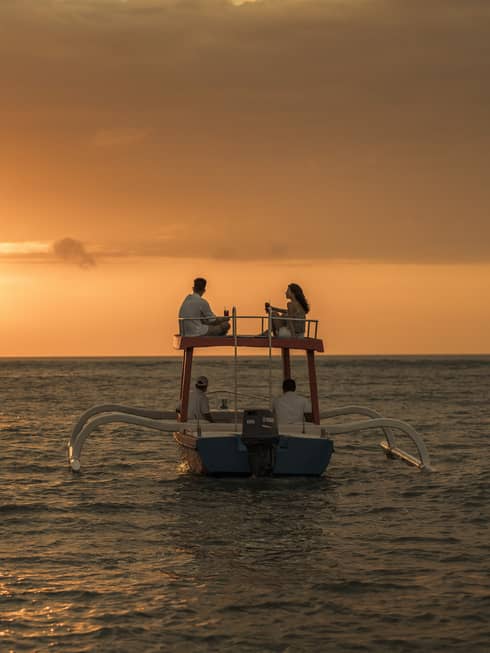 Couple sits on roof of boat sailing on ocean at sunset