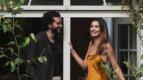 Two people stand on a vine-covered balcony surrounded by foliage.