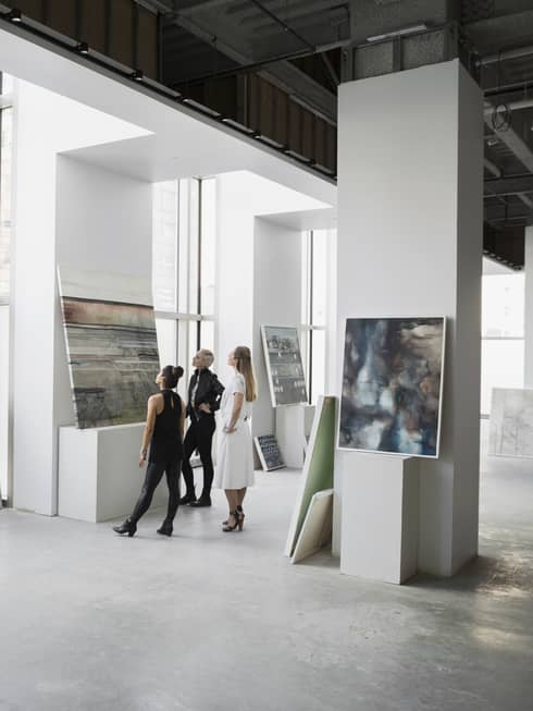 Three women observe art displayed in a gallery