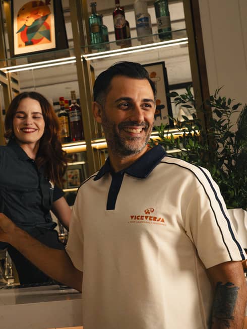 Smiling bartender pours a drink into a glass being held by another smiling person