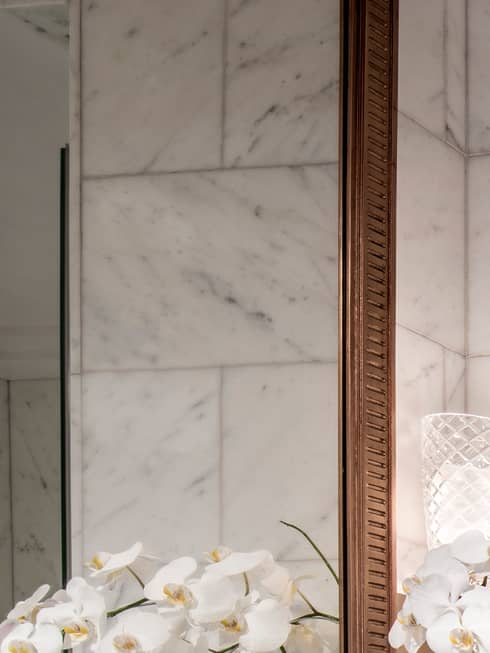 Modern bathroom with grey marble counters, white orchids in vase, glass shower