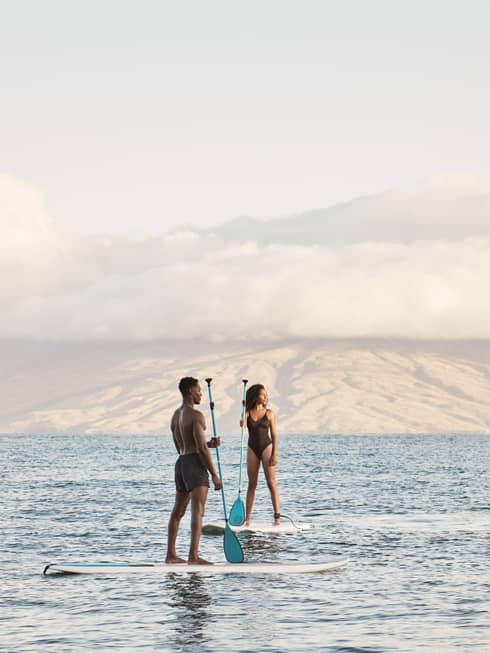 Man and woman stand on SUP paddleboards in the ocean in Maui
