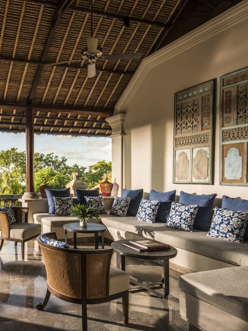 Open-air tropical villa living area with ocean view, rattan furniture, and blue accent pillows.