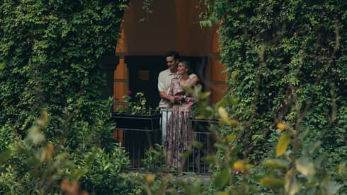 Couple standing on a balcony covered by lush greenery, enjoying a peaceful moment surrounded by nature in an intimate, serene garden setting.