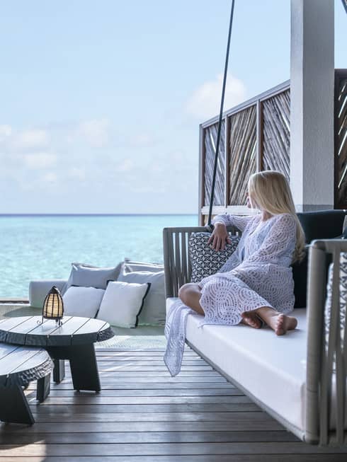 A guest relaxes on a swinging bench on a patio overlooking the ocean