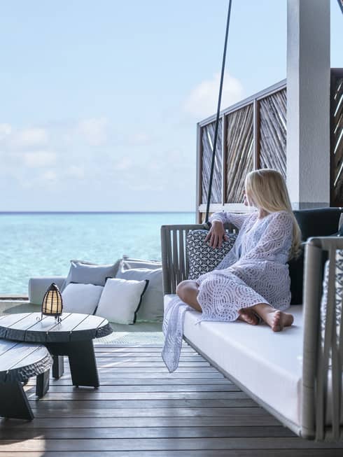 A guest relaxes on a swinging bench on a patio overlooking the ocean
