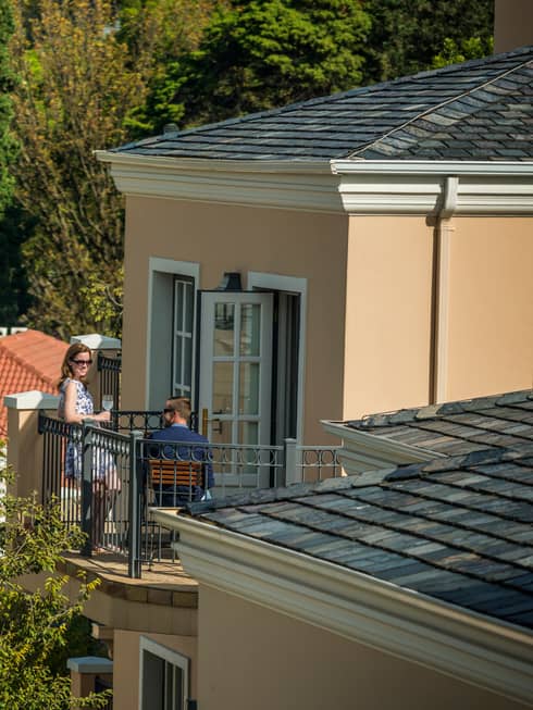 Looking down over corner of hotel roof at man and woman sipping cocktails on sunny balcony