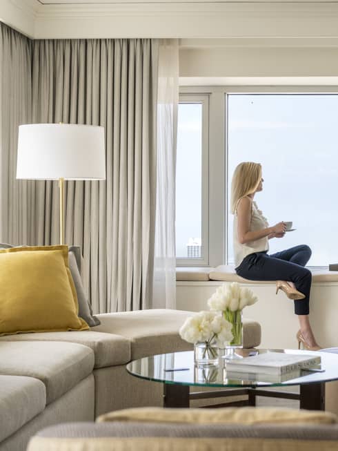 A woman hold a cup of tea and sits on a windowsill in a One Bedroom Suite