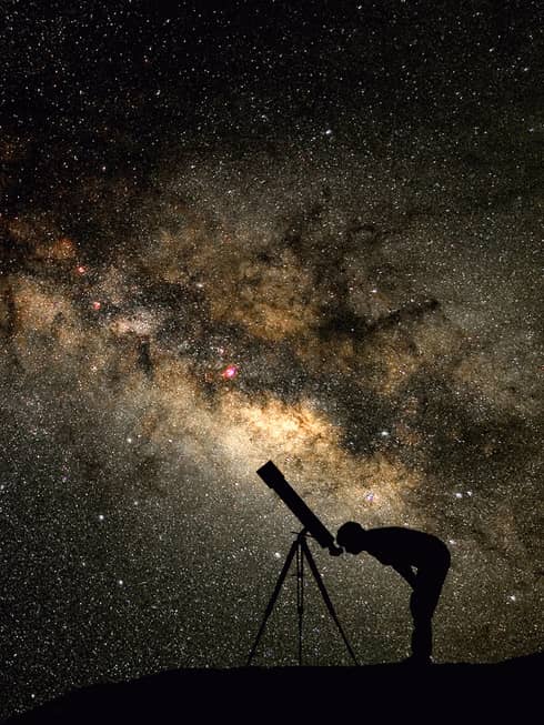 Silhouette of stargazer leaning into telescope against a starry sky, milky way