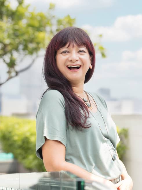 A smiling resident healer Cheryl Rodriguez poses outdoors, downtown Hong Kong looming behind her