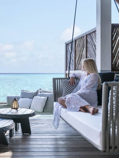 A guest relaxes on a swinging bench on a patio overlooking the ocean