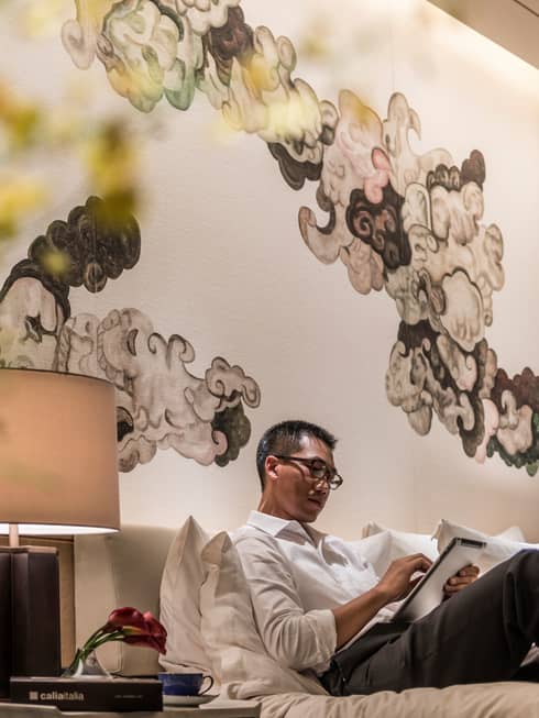 Man lounge on bed, reads iPad under black-and-white Chinese brushwork mural
