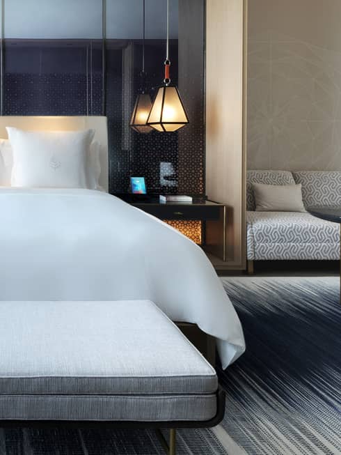 Close-up of modern upholstered chaise with rolled pillow at foot of hotel room bed with white linens