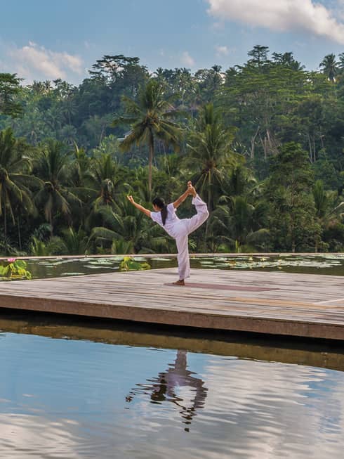 A guest does yoga on the roof of Four Seasons Resort Bali Sayan with a blue sky reflected in the water