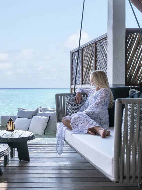 A guest relaxes on a swinging bench on a patio overlooking the ocean