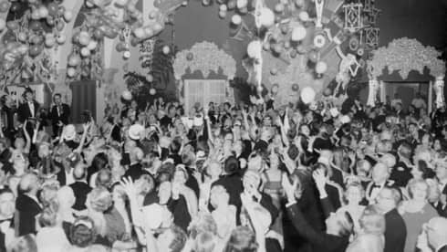 A black and white photo of a large group of people celebrating with balloons in a large room.