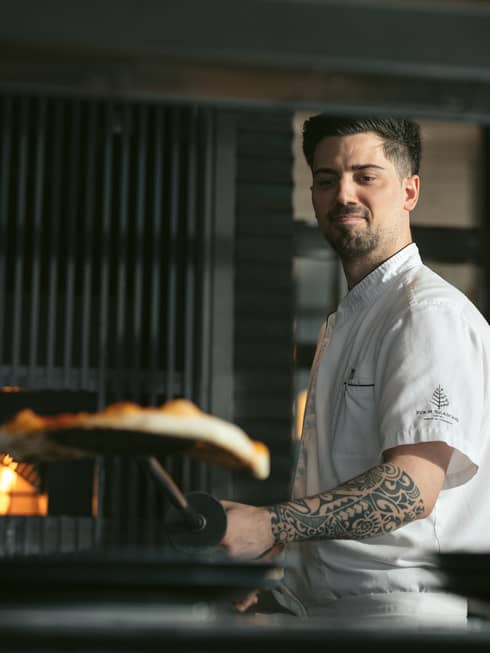 Chef Alessandro de Loe placing a pizza in a large oven